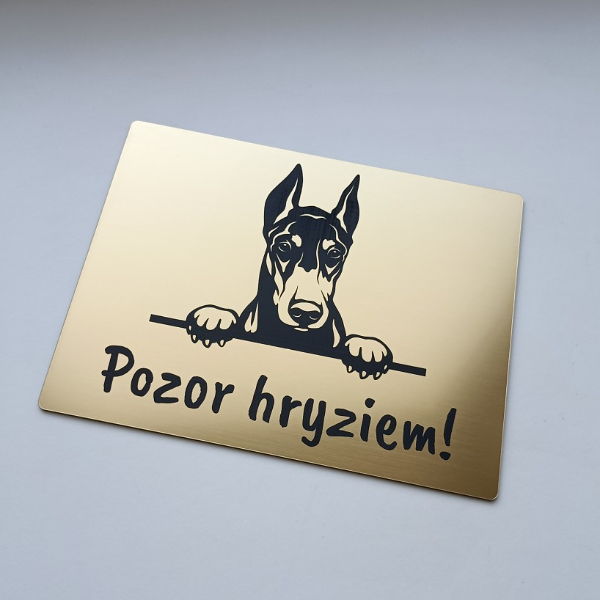 Zlatá tabuľka s vykúkajúcim dobermanom a nápisom Pozor, hryziem