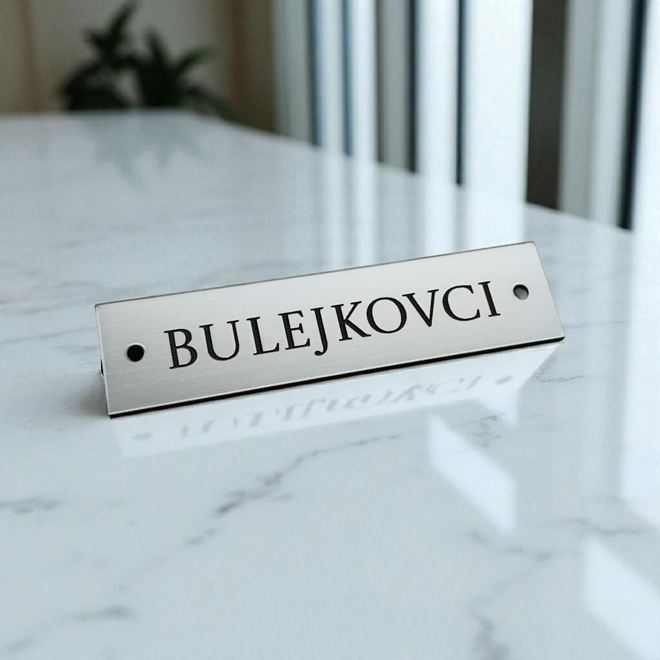 strieborná úzka menovka s dierkami 8 × 2 cm na mramore